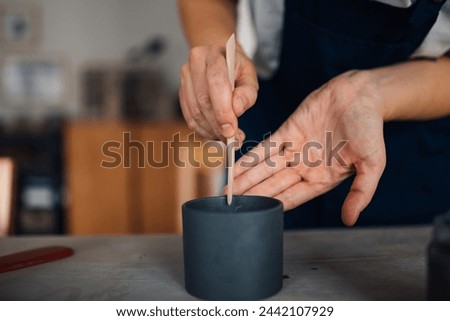 Cropped picture of craftswoman's hands using pottery tool and making handmade ceramic mug made of clay. Close up of unrecognizable ceramist using pottery tool for earthenware making at pottery studio.