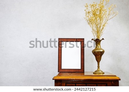 empty picture frame mockup and gypsophila flowers vase on wooden table near grunge wall, autumn fall concept