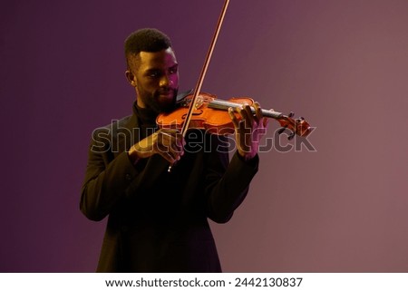 Elegant musician in black suit playing violin against vibrant purple background with skillful finesse Royalty-Free Stock Photo #2442130837