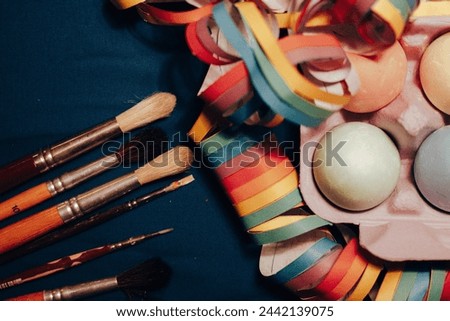 Creative festive holiday background. Painted Easter eggs, paint brushes, colorful tinsel for decor lying on table top view Spring holidays preparation