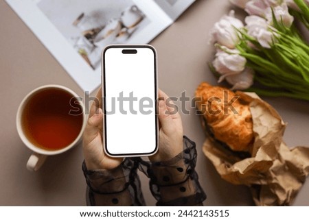 Phone with isolated screen on the background of a cup of tea and a croissant.