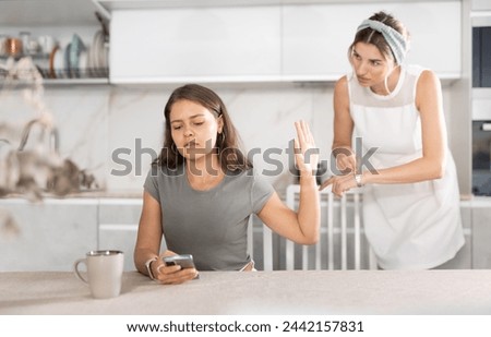 Upset daughter is sitting at table. Mom yells at her daughter in the background
