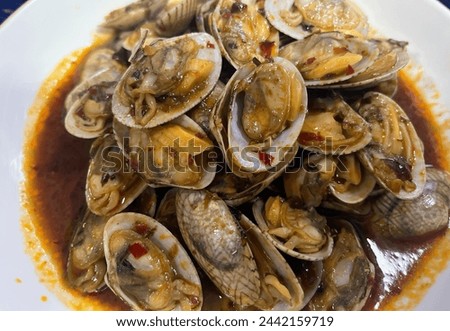 a photography of a plate of clams with sauce and a spoon. Royalty-Free Stock Photo #2442159719