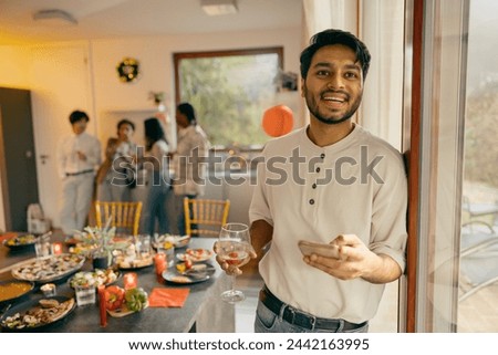 Smiling man with glass of wine and phone standing on friends background at home holiday party