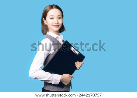 Young Asian businesswoman holding document file in front of blue background.