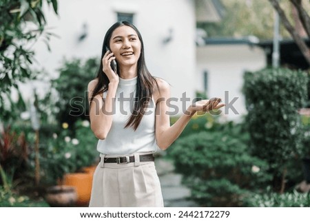 Joyful businesswoman has a pleasant conversation on her phone while walking in a lush garden setting.