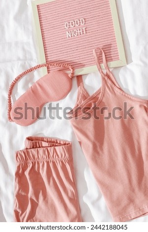 Good night wishes concept, Pink female pajama, sleep eye mask on white cloth bed sheet. Felt board with text, Top view pretty pyjamas for health sleeping. Romance mood, delicate image, flat lay