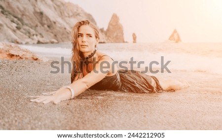 Woman summer travel sea. Happy tourist in black dress enjoy taking picture outdoors for memories. Woman traveler posing on sea beach surrounded by volcanic mountains, sharing travel adventure journey