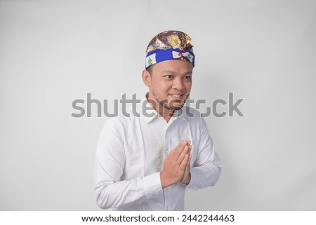 Smiling young Balinese man wearing traditional headdress called udeng doing greeting or welcome gesture, isolated over white background Royalty-Free Stock Photo #2442244463