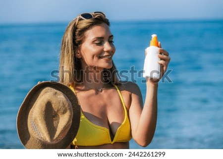 Beautiful young woman putting on sunscreen at the beach.