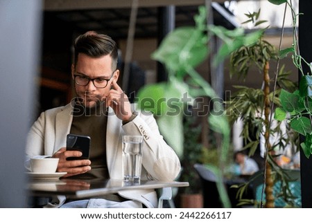 Handsome young businessman looking thoughtful while scrolling his mobile phone at coffee shop.