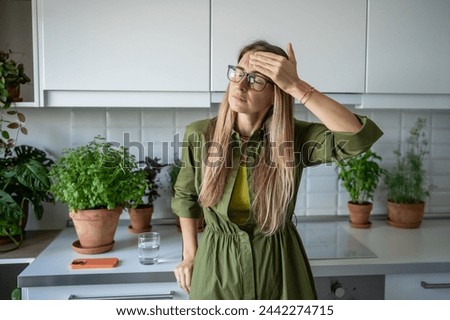 Tired exhausted blonde woman feels headache touching head with closed eyes on kitchen at home. Unhealthy female in glasses suffers head pain, dizziness, migraine, cephalalgia feeling unwell pressure. Royalty-Free Stock Photo #2442274715