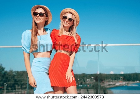Two young beautiful smiling hipster women in trendy summer same clothes. Carefree models posing in the street. Positive models having fun. Cheerful and happy, at sunny day. In hat and sunglasses