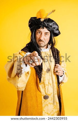 A man in a period costume resembling Christopher Columbus points forward authoritatively, with elaborate garb set against a bold yellow background. Royalty-Free Stock Photo #2442303955