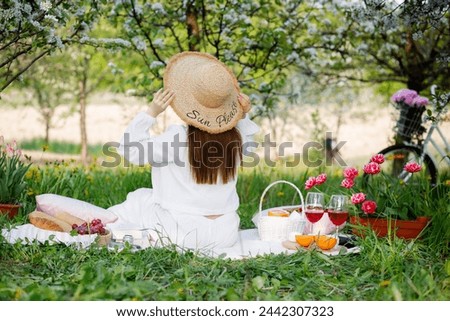 A girl on a picnic in a blooming garden. Easter is coming soon. Lots of sweets and fruits on the cover. Green grass. May