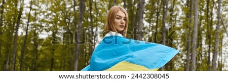Back view of female young blonde hiker, holding the Ukrainian flag and turning to camera, banner
