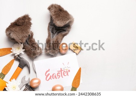 Composition with greeting card, bunny ears, construction tools and Easter eggs on light background