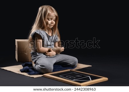 Homeless little girl with picture of house on dark background