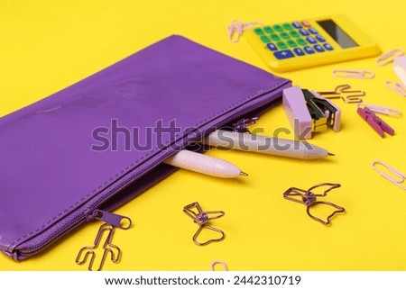 Purple pencil case and different stationery on yellow background