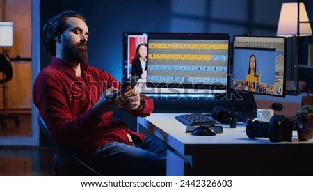 Photographer uses retouching software to edit pictures on computer monitors, taking a break after working too much. Photo editor tired after doing color grading on images, relaxing by using smartphone