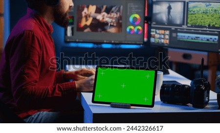 Green screen tablet on desk in multimedia agency next to video editor working for independent production company inputting music, dialogues, graphics and effects over raw footage