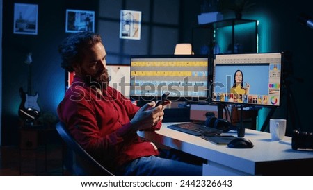 Photographer taking break from using photo editing software on PC display, texting friends to relax. Freelancer stops using photographs retouching program to spend time on mobile phone