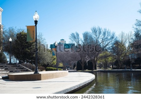 Light pole banner and buildings along Bricktown canal with curved sidewalk pathway, riverside restaurants, tourist attractions in Entertainment District landmarks, travel destination, water taxi. USA