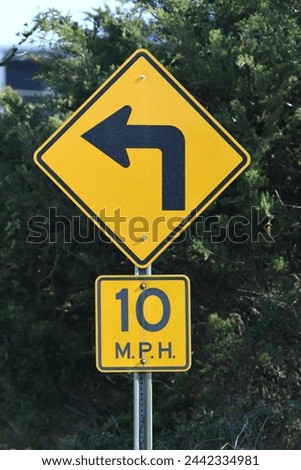 A yellow and black traffic sign with an arrow pointing to or indicating a left hand turn. The image also contains a 10 M.P.H. sign on the same signpost. There is also a dark green background.