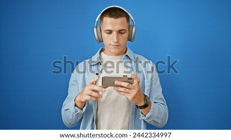 Hispanic man in casual attire using smartphone with headphones against blue background outdoor