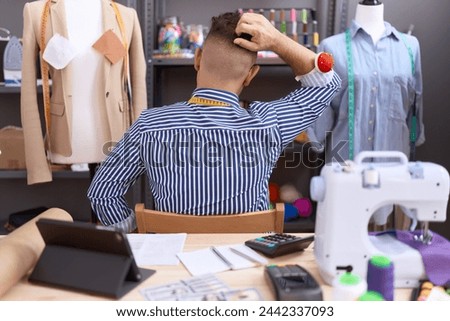 Hispanic man with beard dressmaker designer working at atelier backwards thinking about doubt with hand on head  Royalty-Free Stock Photo #2442337093