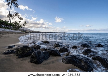 Waves from the Pacific Ocean gently wash over volcanic rocks on the shores of Kaanapali Beach in Lahaina, Hawaii on the island of Maui. Royalty-Free Stock Photo #2442341853