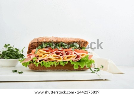 Sandwich. One fresh big submarine sandwich with ham, cheese, lettuce, tomatoes and microgreens on light background. Healthy breakfast theme concept, school lunch, breakfast or snack. 