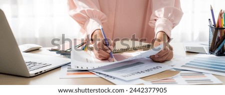Professional interior designer compares color palette between laptop and document with color palette and color swatches scatter around. Creative design and working concept. Variegated.