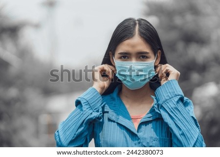 Close-up of Asian woman face wearing blue medical mask for dust and virus infection prevention, outdoor, pollution.