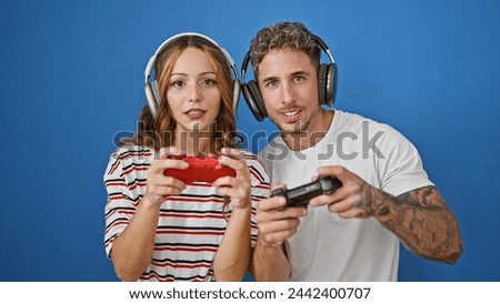 A man and a woman wearing headphones play video games together against a blue background, showcasing leisure and technology.