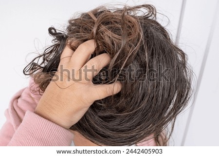woman scratching brown hair, feeling itchy and possibly having lice, showing effects of infestation, Medical conditions, Pediculosis, itching and irritation
