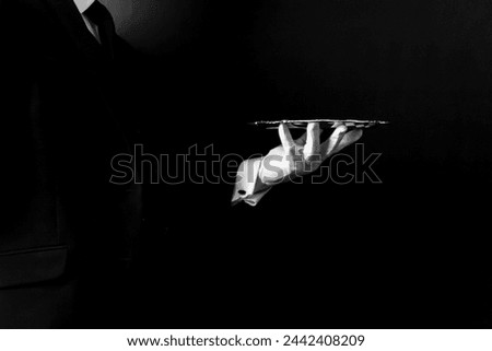 Portrait of Formal Butler or Waiter in Dark Suit and White Gloves Holding Serving Tray. Service Industry and Professional Hospitality. Royalty-Free Stock Photo #2442408209