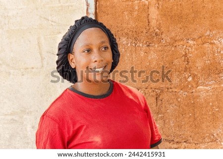single african young woman with headwear standing in front of the house in a village, Royalty-Free Stock Photo #2442415931
