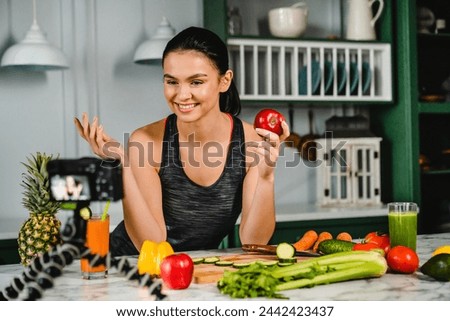Cheerful young caucasian woman food blogger talking about fruits on the camera in the kitchen. Female athlete broadcasting live to audience about slimming and dieting eating habits