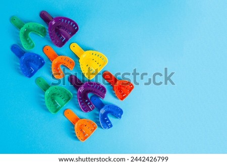 Multi-colored dental spoons for taking an impression of the dental jaw on a blue background. Making an impression of the jaw for braces and dental prosthetics. Royalty-Free Stock Photo #2442426799