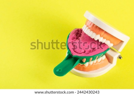 Green dental spoon for taking a dental impression in a mock-up of a dental jaw on a yellow background. Making an artificial jaw for malocclusion. Manufacturing of dental prostheses, orthodontics in Royalty-Free Stock Photo #2442430243