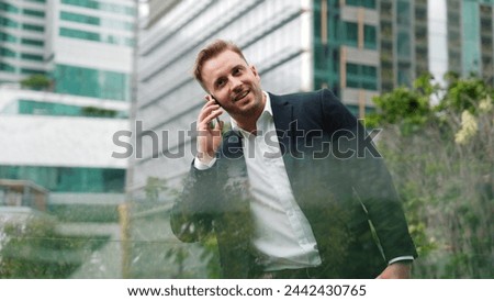 Successful businessman standing at rooftop while talking with marketing team about investment by using phone. Caucasian investor enjoy relaxing by looking at modern skyscraper view. Lifestyle. Urbane