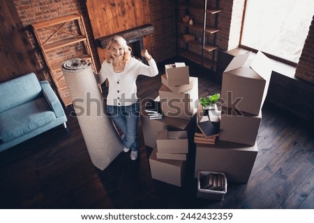 Full body photo of aged lady hold carpet raise fist achieve wear white cardigan loft interior house indoors