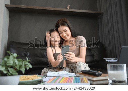 Beautiful Asian mother working at home and taking care of cute little daughter