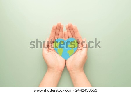 World heart day. Flat lay of hands holding heart shape with earth map made by paper on green background. Template for cardiology medical care, earth's day celebration, love and save the earth.