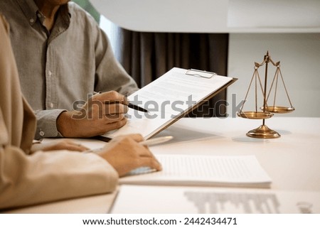 Lawyer and client are listening and giving advice about a legal case on the work desk of a law firm with a gavel and a scale.
