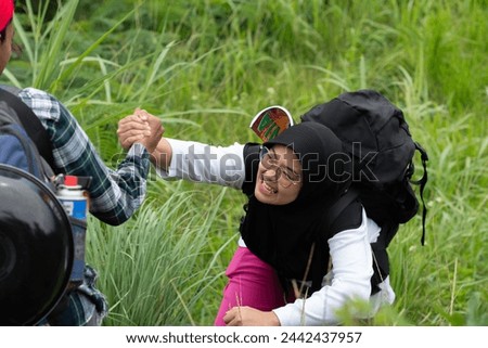 Man's hand gives help to young Asian Muslim woman while climbing a mountain together, helping and working together
