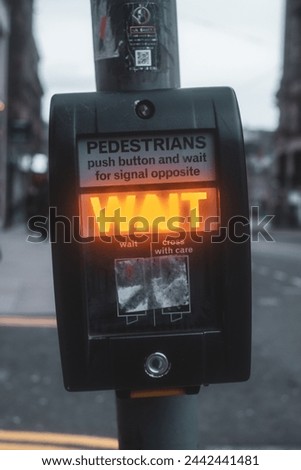 Photo of a traffic signal at a crosswalk in the city of Edinburgh. It has a button and an illuminated sign that says "Wait".
