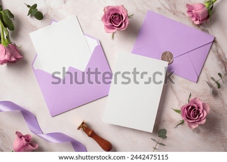 Blank white paper card, violet envelopes, roses on marble background. Flat lay, top view, copy space. Wedding invitation card design.