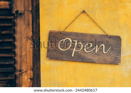 Rustic wooden Open sign hanging. A warm, inviting rustic wooden 'Open' sign adorns a vibrant yellow stucco wall.